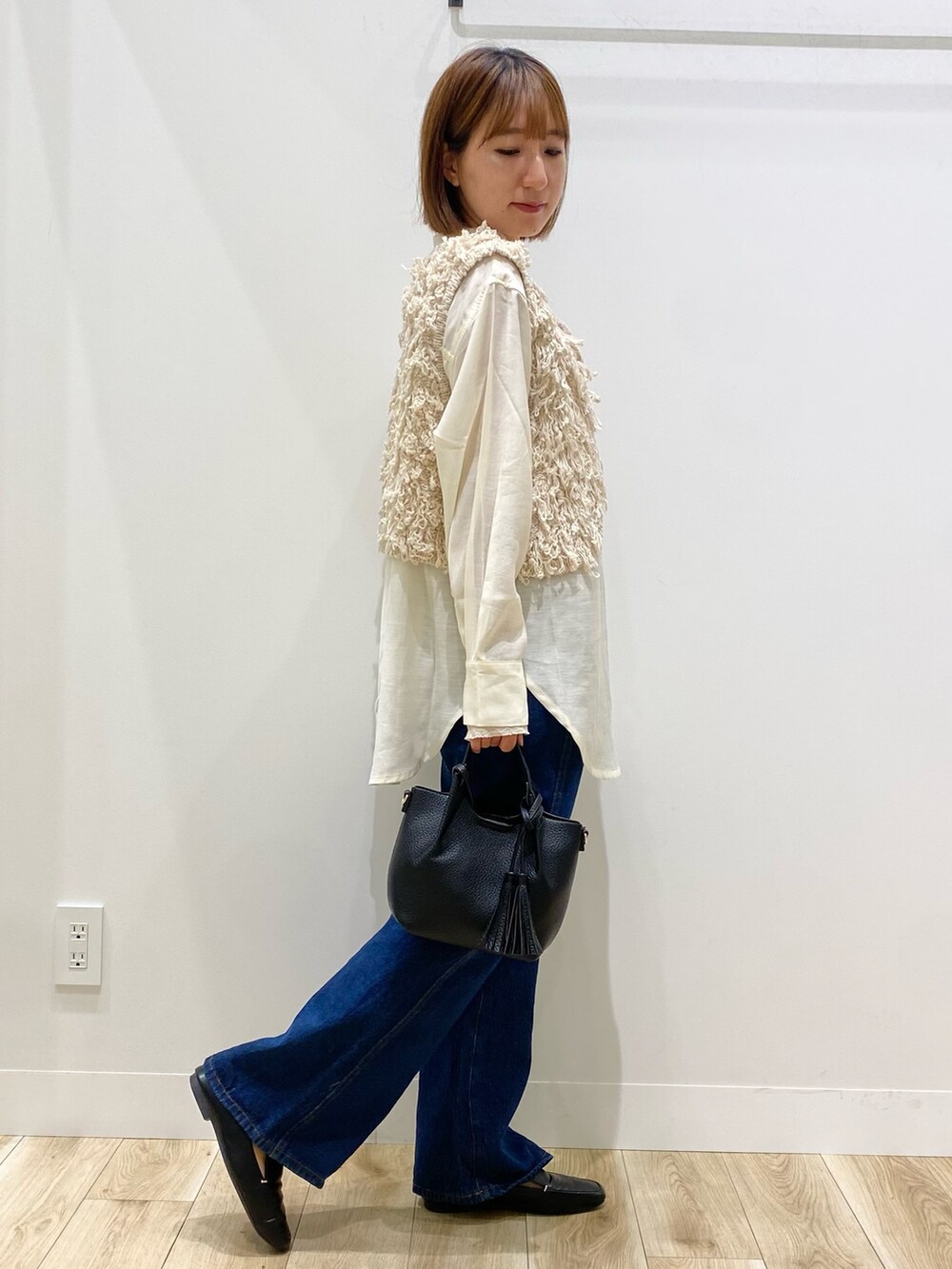 ベージュ系のベスト、ブルー系のデニムパンツ、ブラック系のショルダーバッグを着用したレディースの秋コーディネートの2枚目の写真