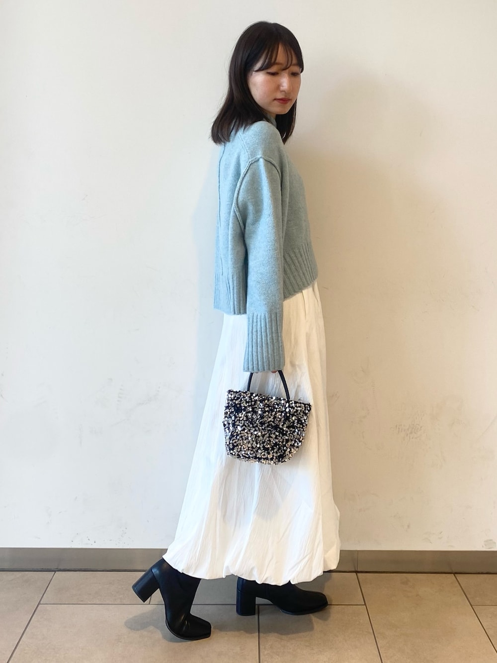 ホワイト系のスカート、ブルー系のニット/セーター、ブラック系のブーツを着用したレディースの冬コーディネートの2枚目の写真