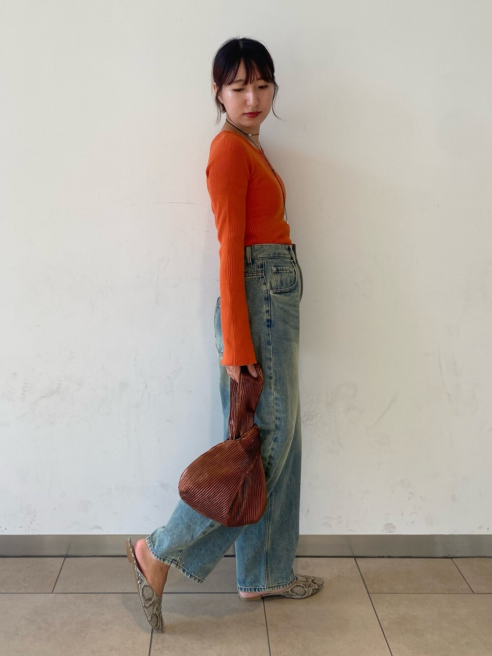 ブルー系のデニムパンツ、オレンジ系のニット/セーター、ブラウン系のハンドバッグを着用したレディースの秋コーディネートの2枚目の写真