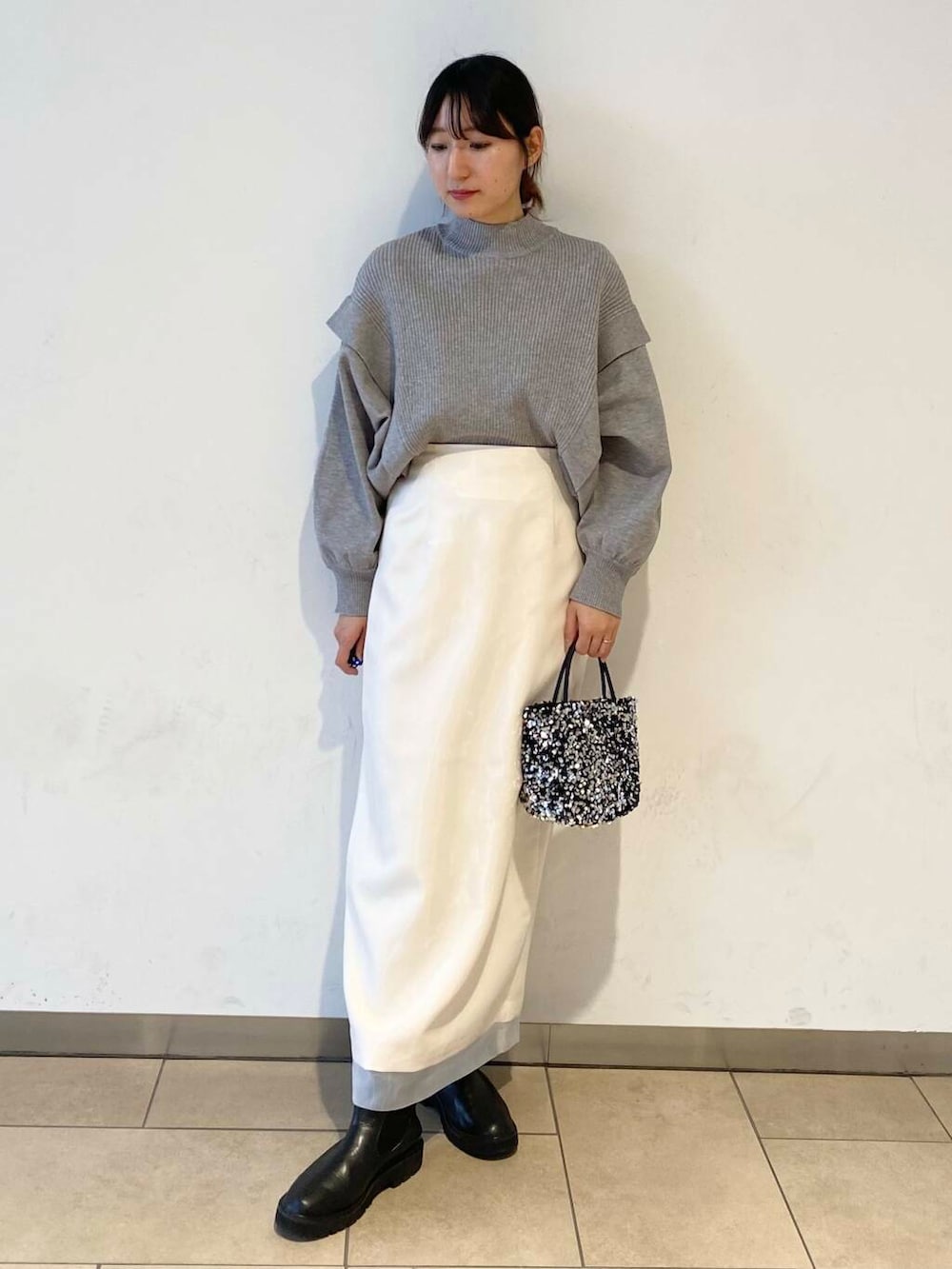 ブラック系のブーツ、グレー系のニット/セーター、ホワイト系のスカートを着用したレディースの冬コーディネートの2枚目の写真