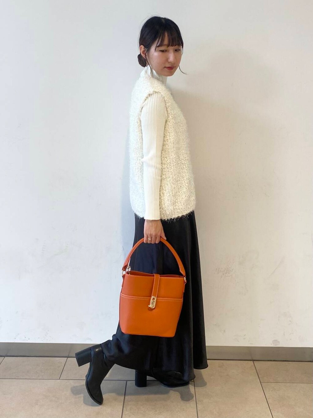 ホワイト系のニット/セーター、オレンジ系のハンドバッグ、ブラック系のブーツを着用したレディースの秋コーディネートの2枚目の写真