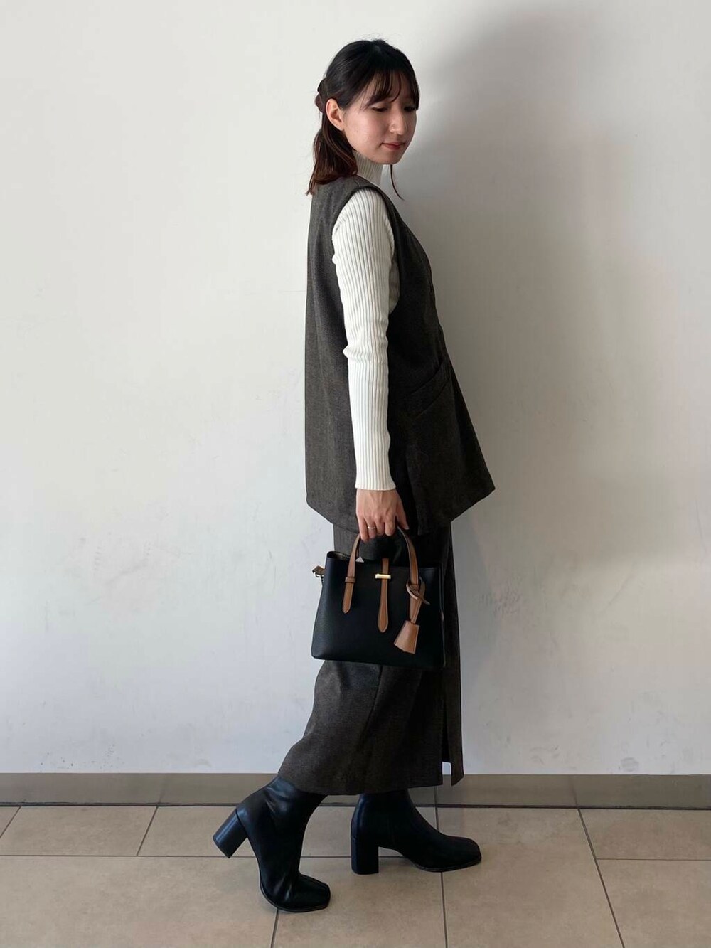 ブラック系のハンドバッグ、ホワイト系のニット/セーター、ブラック系のブーツを着用したレディースの冬コーディネートの2枚目の写真