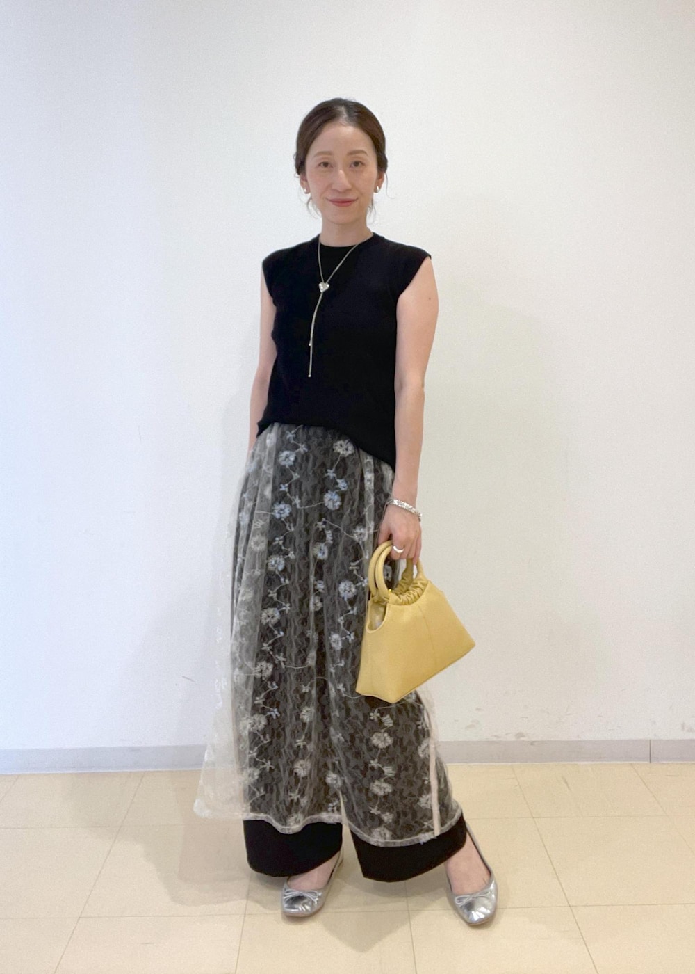ブラック系のニット/セーター、イエロー系のショルダーバッグ、ホワイト系のスカートを着用したレディースの夏コーディネートの2枚目の写真