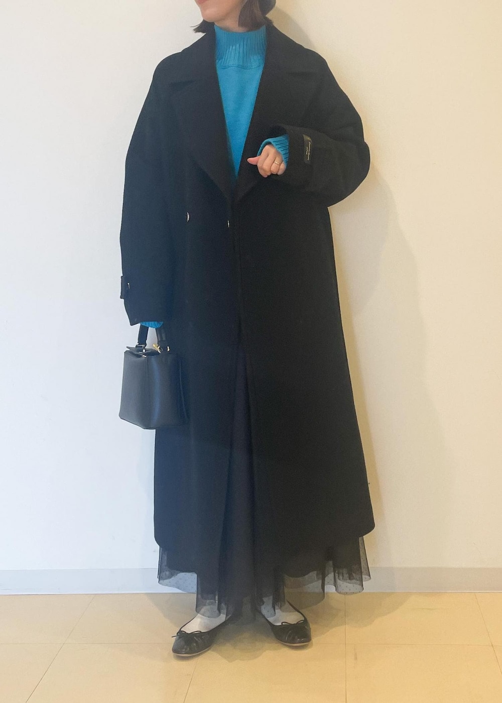 ブルー系のニット/セーター、ブラック系のスカート、ブラック系のチェスターコートを着用したレディースの秋コーディネートの2枚目の写真