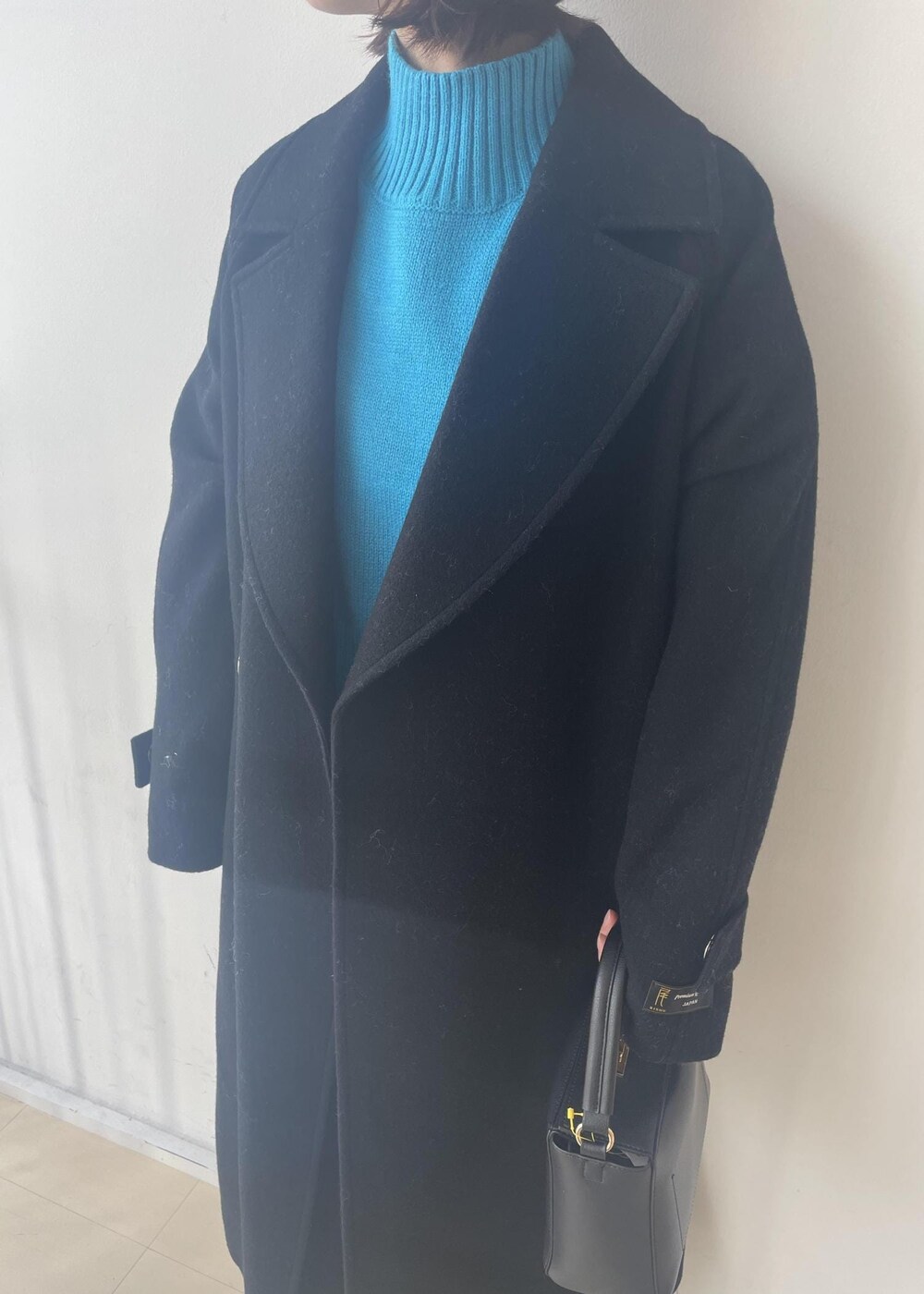 ブルー系のニット/セーター、ブラック系のスカート、ブラック系のチェスターコートを着用したレディースの秋コーディネートの3枚目の写真