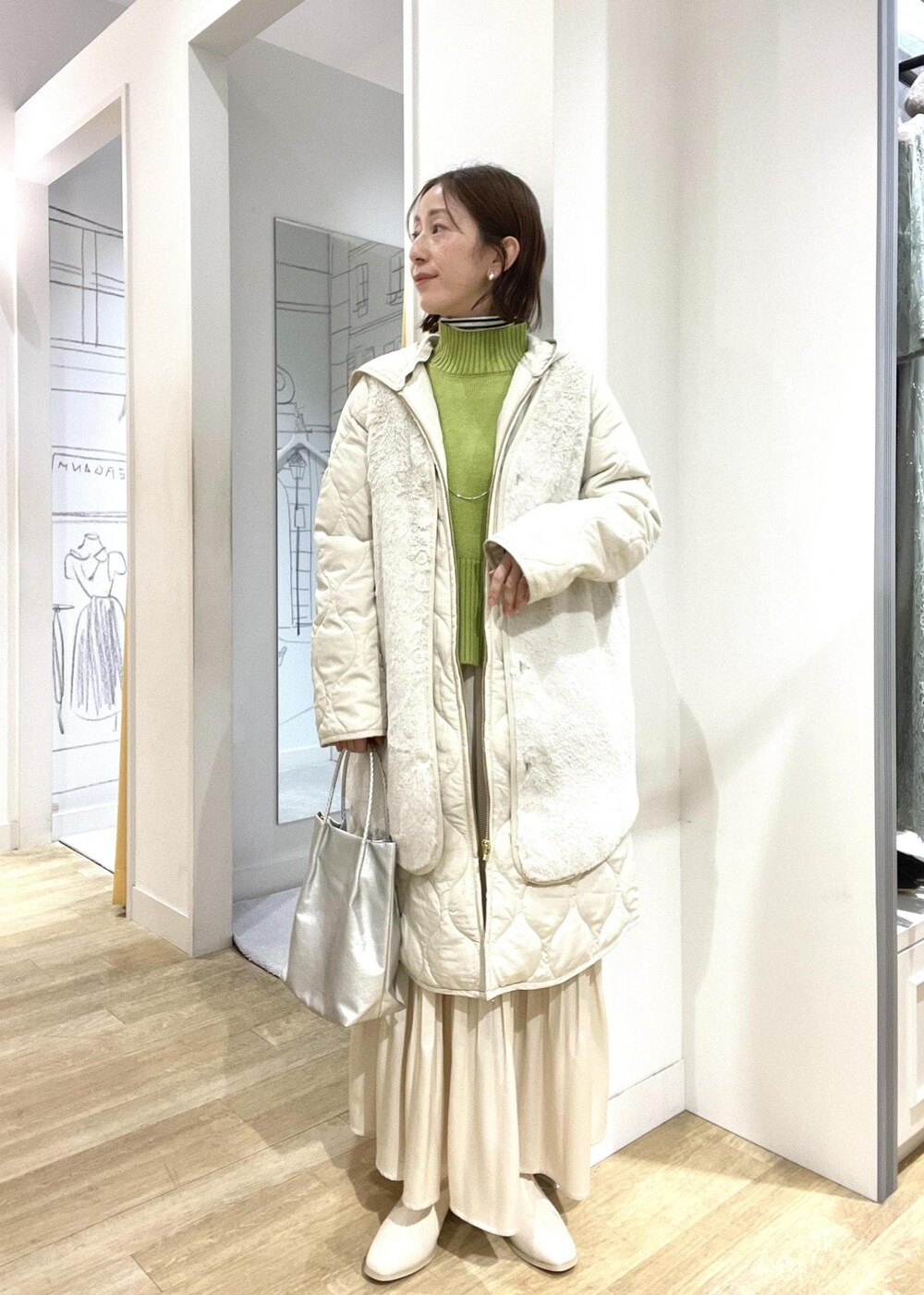 シルバー系のトートバッグ、グリーン系のニット/セーター、ホワイト系のブーツを着用したレディースの冬コーディネートの3枚目の写真