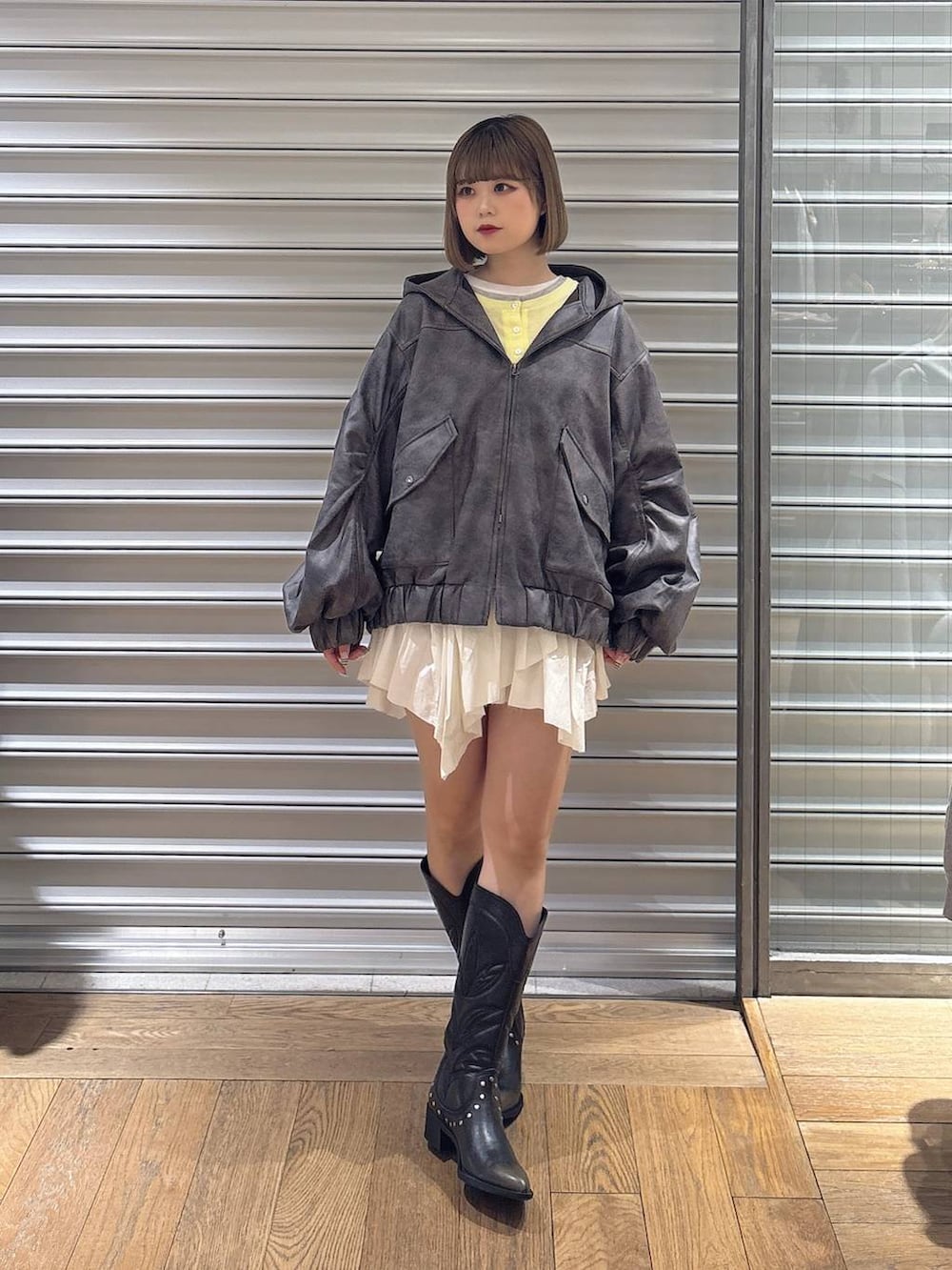 ブラック系のブーツ、グレー系のブルゾン、ホワイト系のスカートを着用したレディースの春コーディネートの2枚目の写真