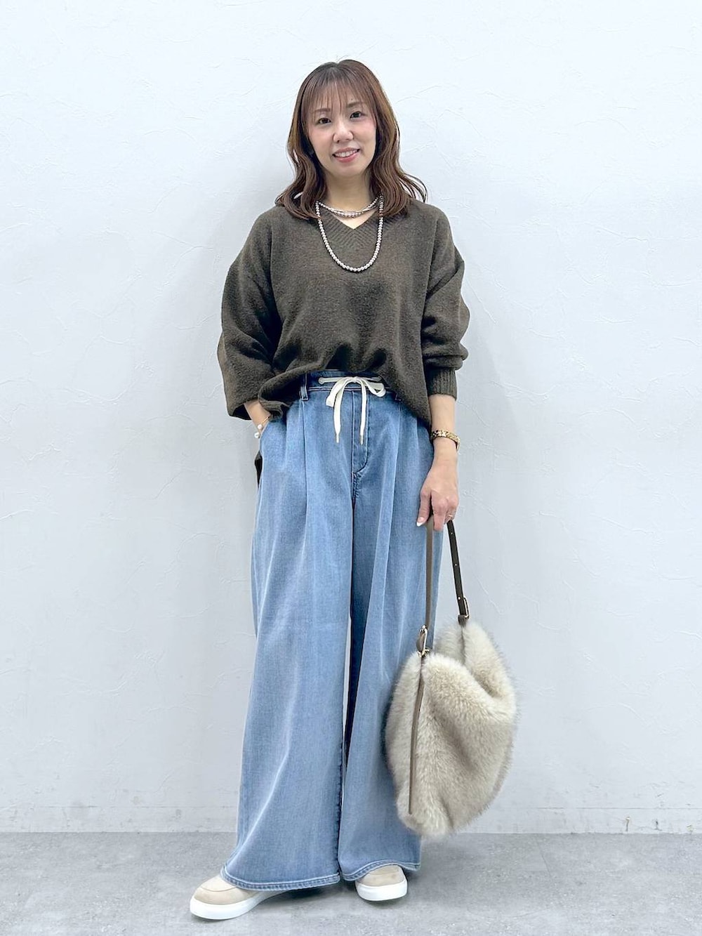 ベージュ系のハンドバッグ、ベージュ系のローファー、ブルー系のデニムパンツを着用したレディースの冬コーディネートの2枚目の写真