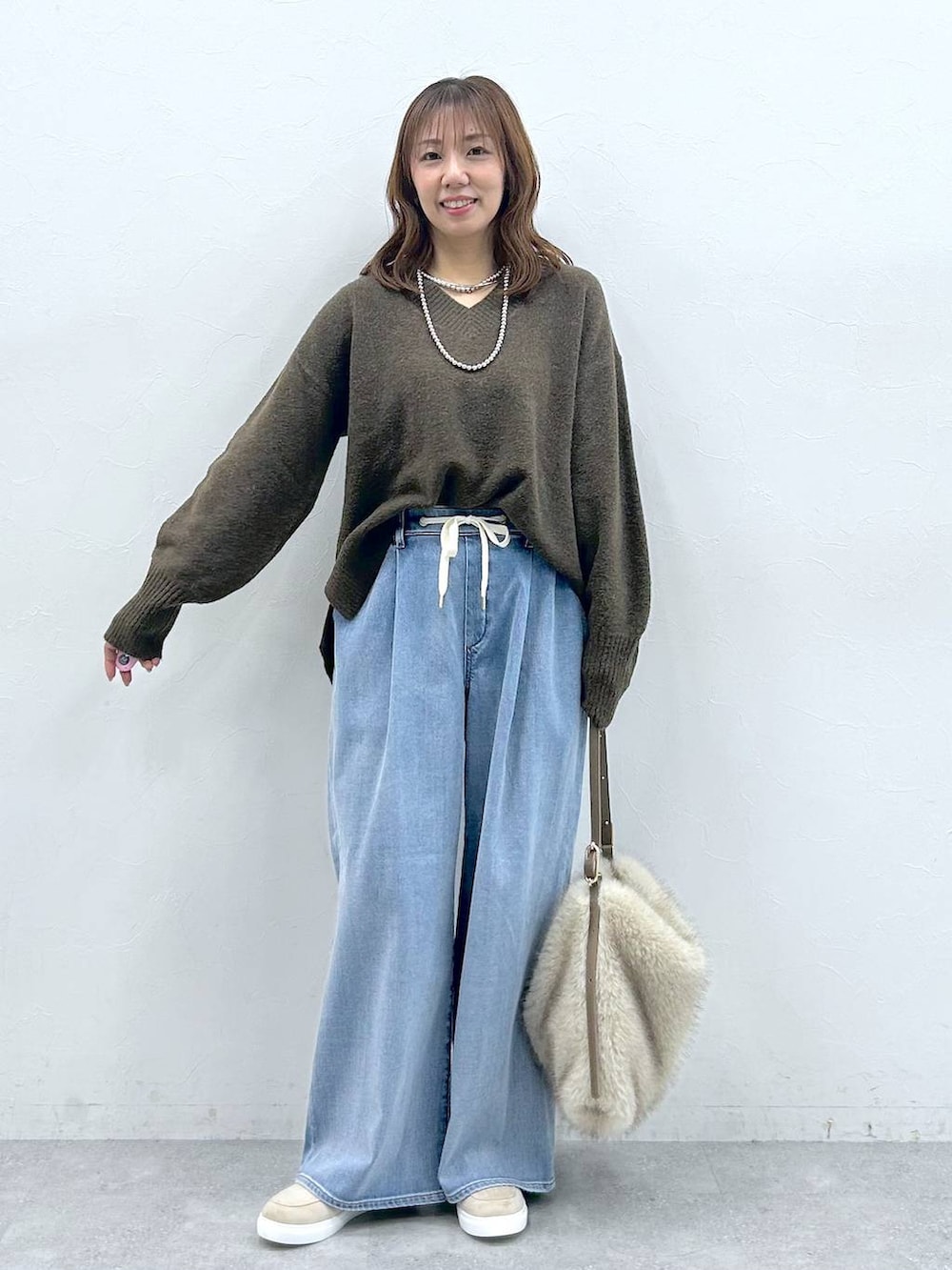 ベージュ系のハンドバッグ、ベージュ系のローファー、ブルー系のデニムパンツを着用したレディースの冬コーディネートの6枚目の写真