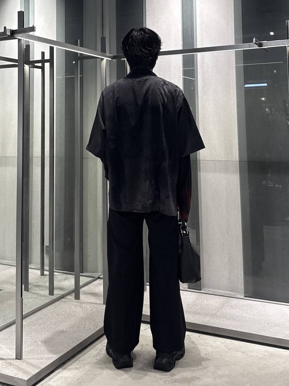 ブラック系のスラックス、オレンジ系のTシャツ/カットソー、ブラック系のスニーカーを着用したメンズの秋コーディネートの2枚目の写真