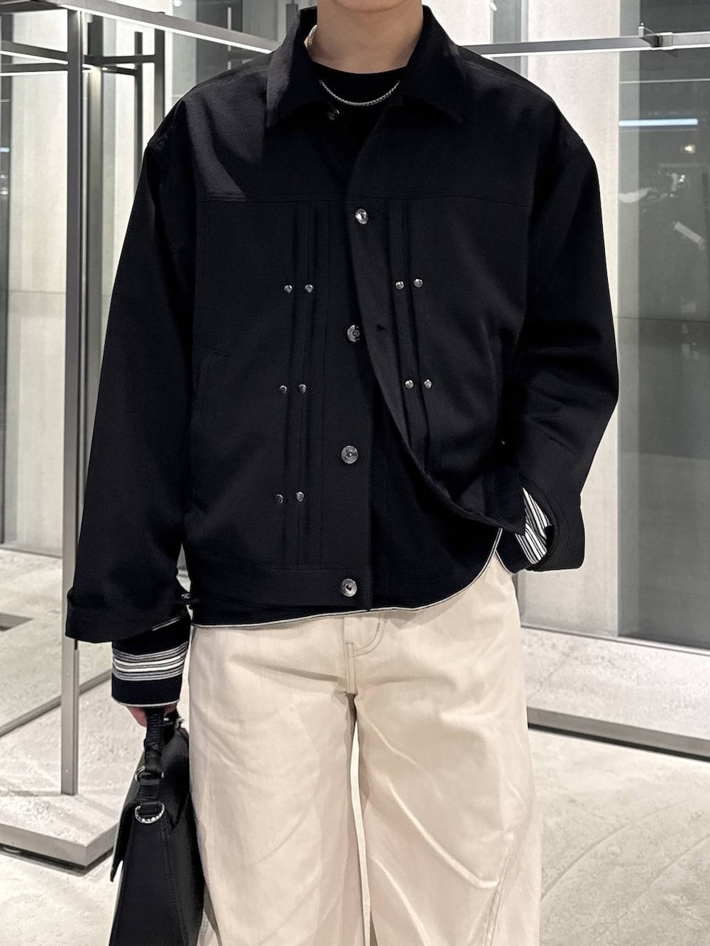 ホワイト系のデニムパンツ、ブラック系のドレスシューズ、ブラック系のブルゾンを着用したメンズの春コーディネートの3枚目の写真