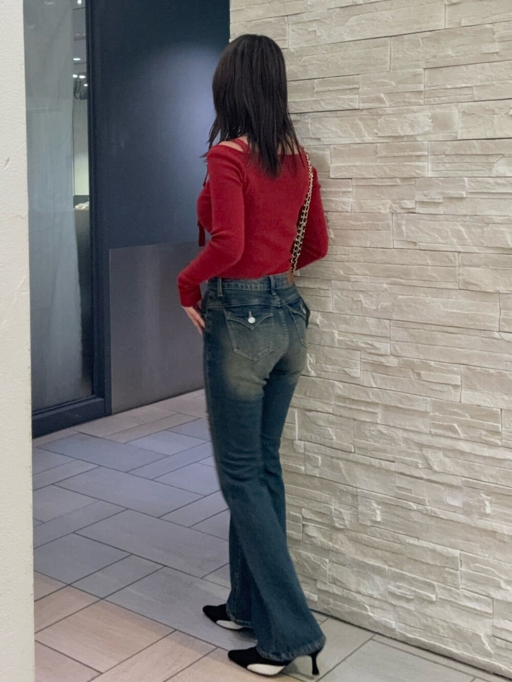 レッド系のニット/セーター、ブルー系のデニムパンツ、ブラック系のパンプスを着用したレディースの秋コーディネートの2枚目の写真