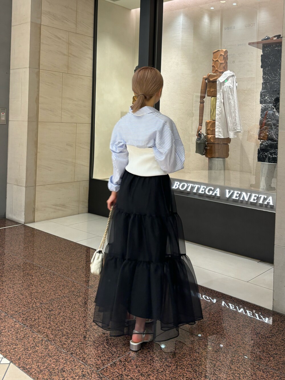 ブラック系のスカート、ホワイト系のニット/セーター、ホワイト系のショルダーバッグを着用したレディースの夏コーディネートの2枚目の写真