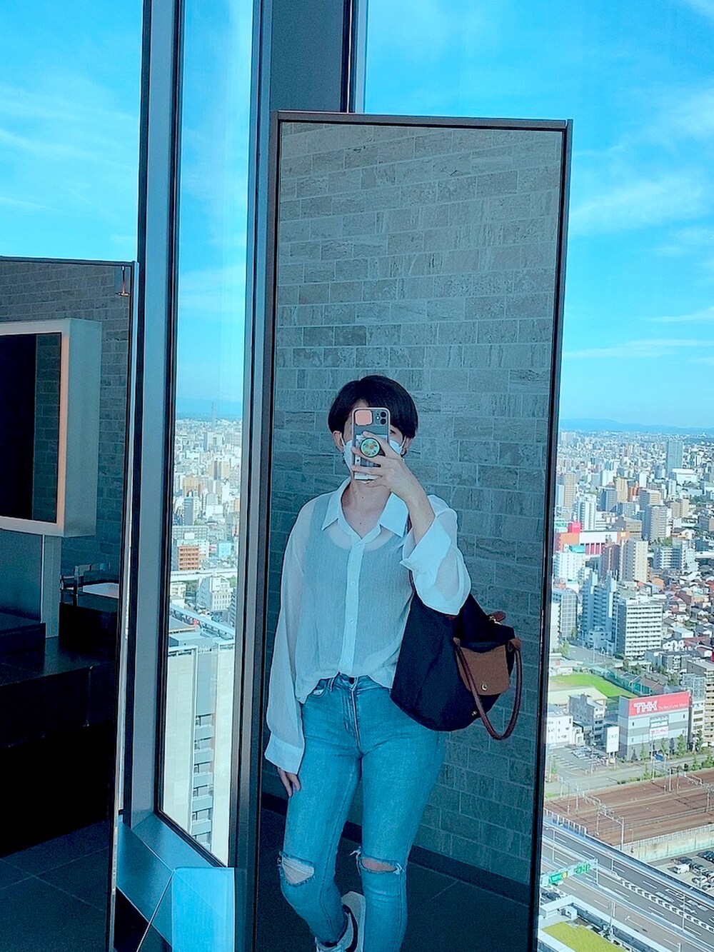 ブラック系のハンドバッグ、ブルー系のデニムパンツを着用したレディースの夏コーディネートの2枚目の写真