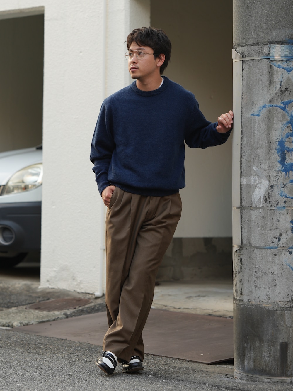 ブラック系のローファー、ブルー系のニット/セーター、ブラウン系のスラックスを着用したメンズの秋コーディネートの2枚目の写真