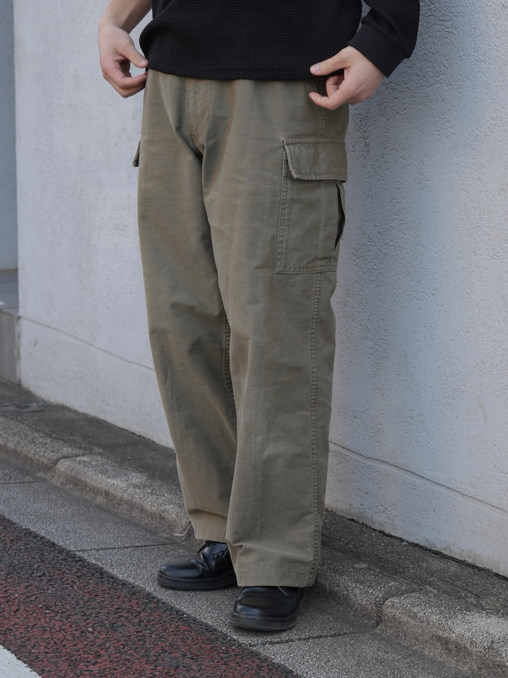 グリーン系のパンツ、ブラック系のドレスシューズ、ブラック系のトップスを着用したメンズの春コーディネートの3枚目の写真
