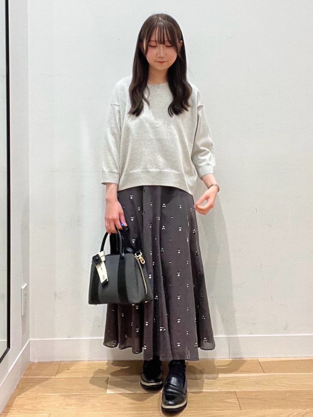 ブラック系のハンドバッグ、ベージュ系のTシャツ/カットソー、グレー系のスカートを着用したレディースの春コーディネートの2枚目の写真