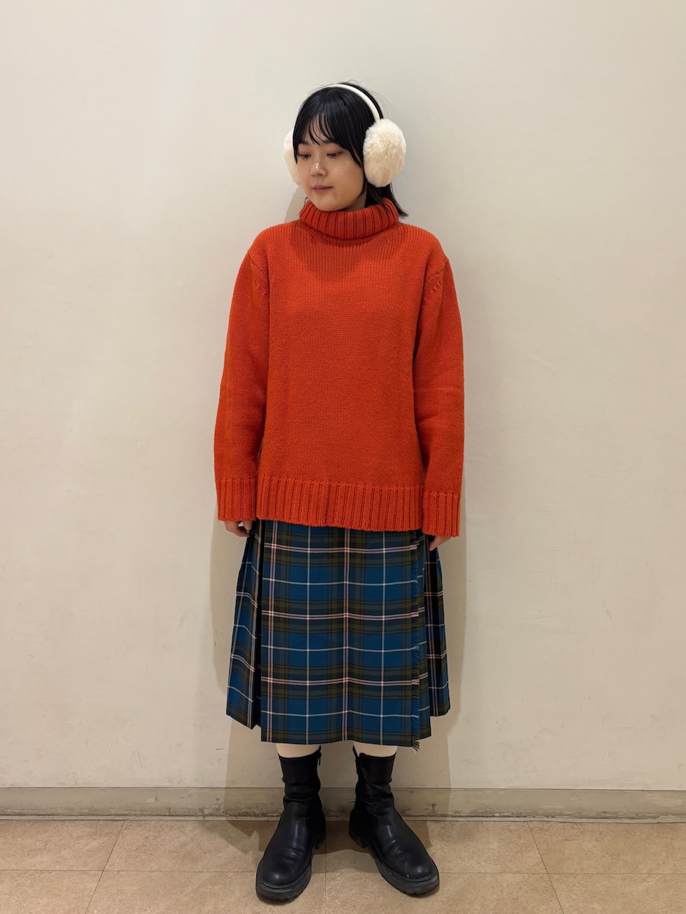 オレンジ系のニット/セーター、ブルー系のスカート、ホワイト系のイヤーマフを着用したレディースの秋コーディネートの2枚目の写真