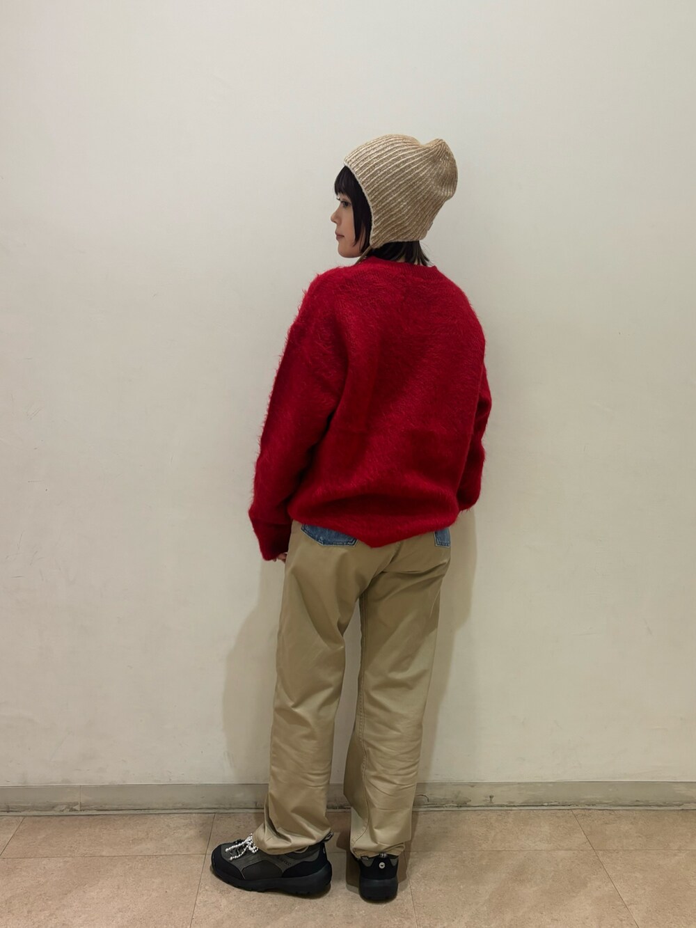 レッド系のニット/セーター、ブルー系のチノパンツ、ベージュ系のニットキャップ/ビーニーを着用したレディースの秋コーディネートの2枚目の写真