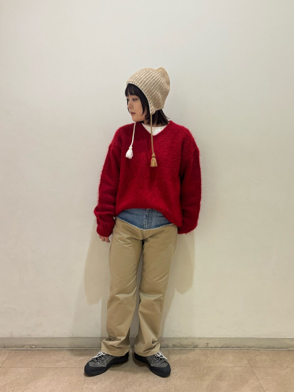 レッド系のニット/セーター、ブルー系のチノパンツ、ベージュ系のニットキャップ/ビーニーを着用したレディースの秋コーディネートの3枚目の写真