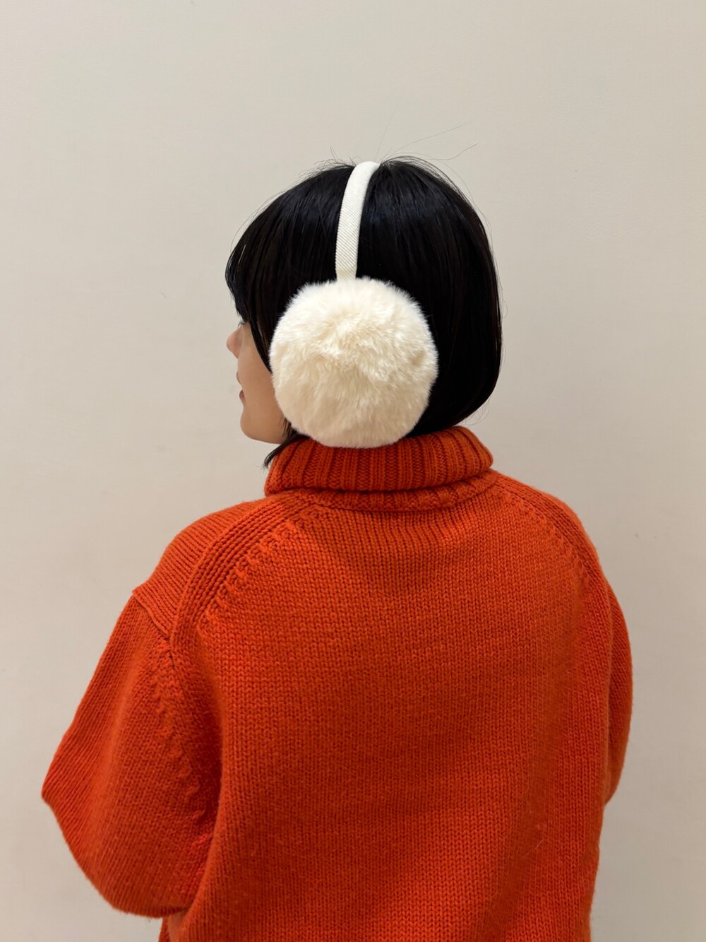 オレンジ系のニット/セーター、ブルー系のスカート、ホワイト系のイヤーマフを着用したレディースの秋コーディネートの5枚目の写真