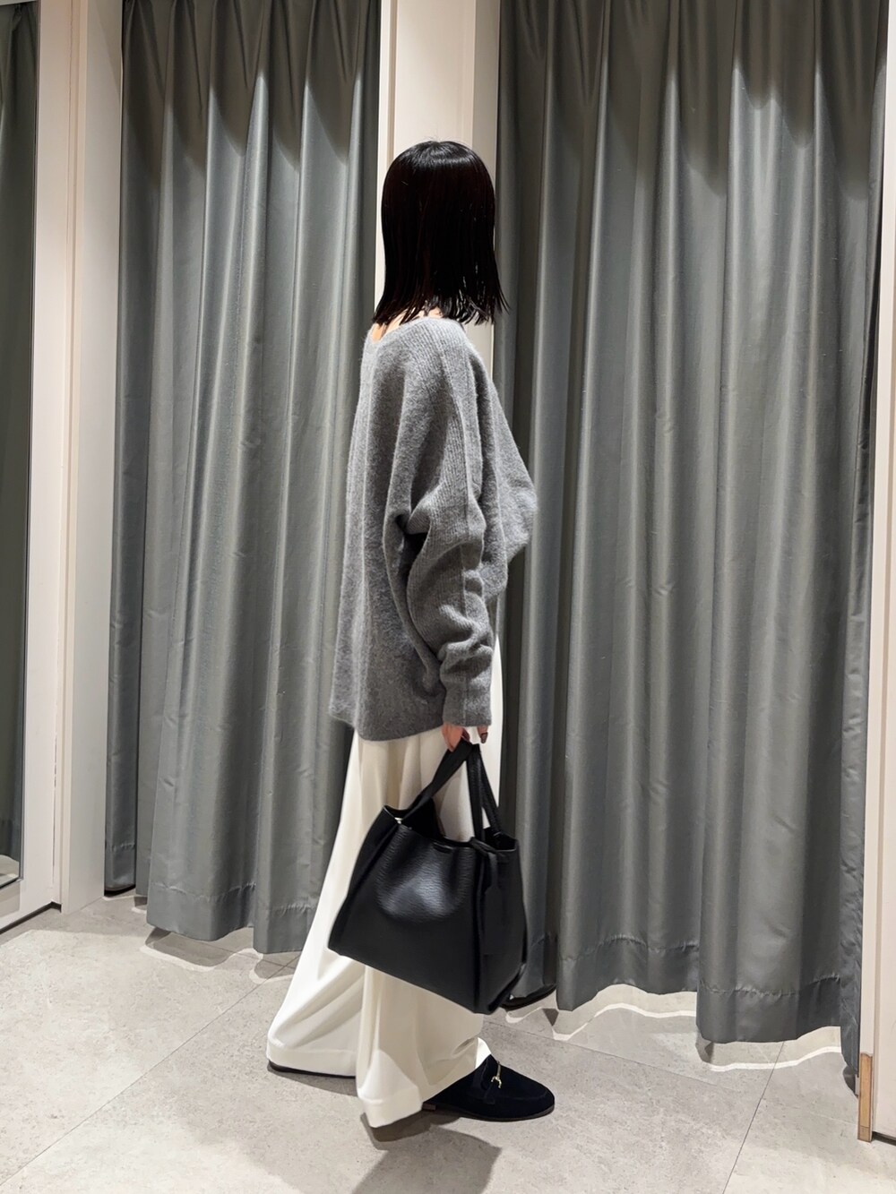 ホワイト系のスラックス、グレー系のニット/セーター、ブラック系のハンドバッグを着用したレディースの冬コーディネートの2枚目の写真