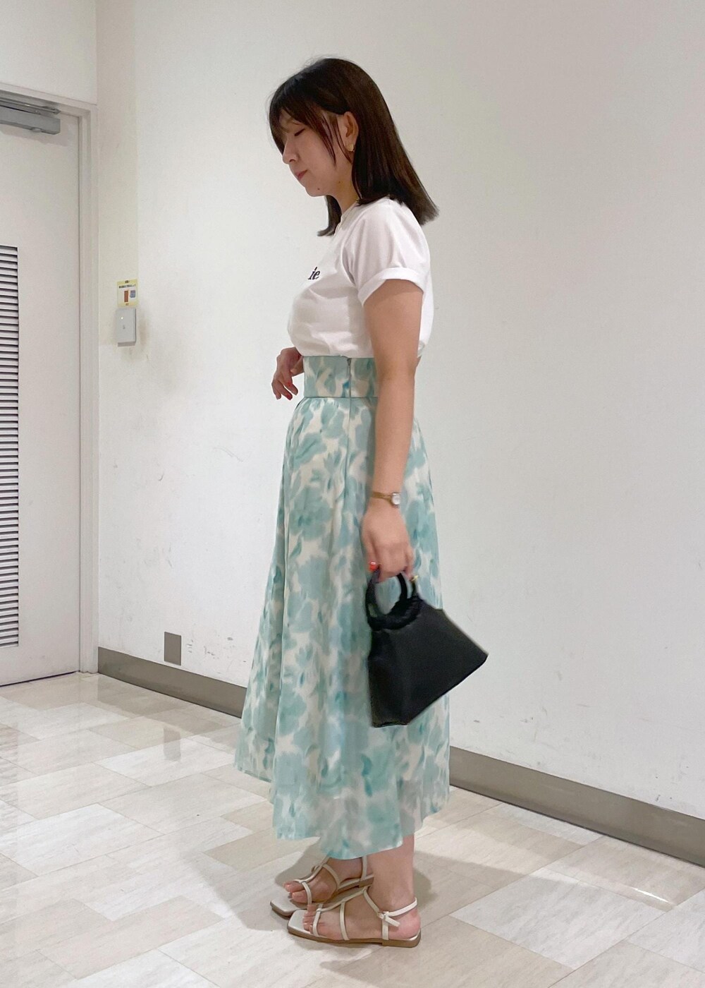 ブルー系のスカート、ブラック系のショルダーバッグ、ホワイト系のTシャツ/カットソーを着用したレディースの夏コーディネートの3枚目の写真