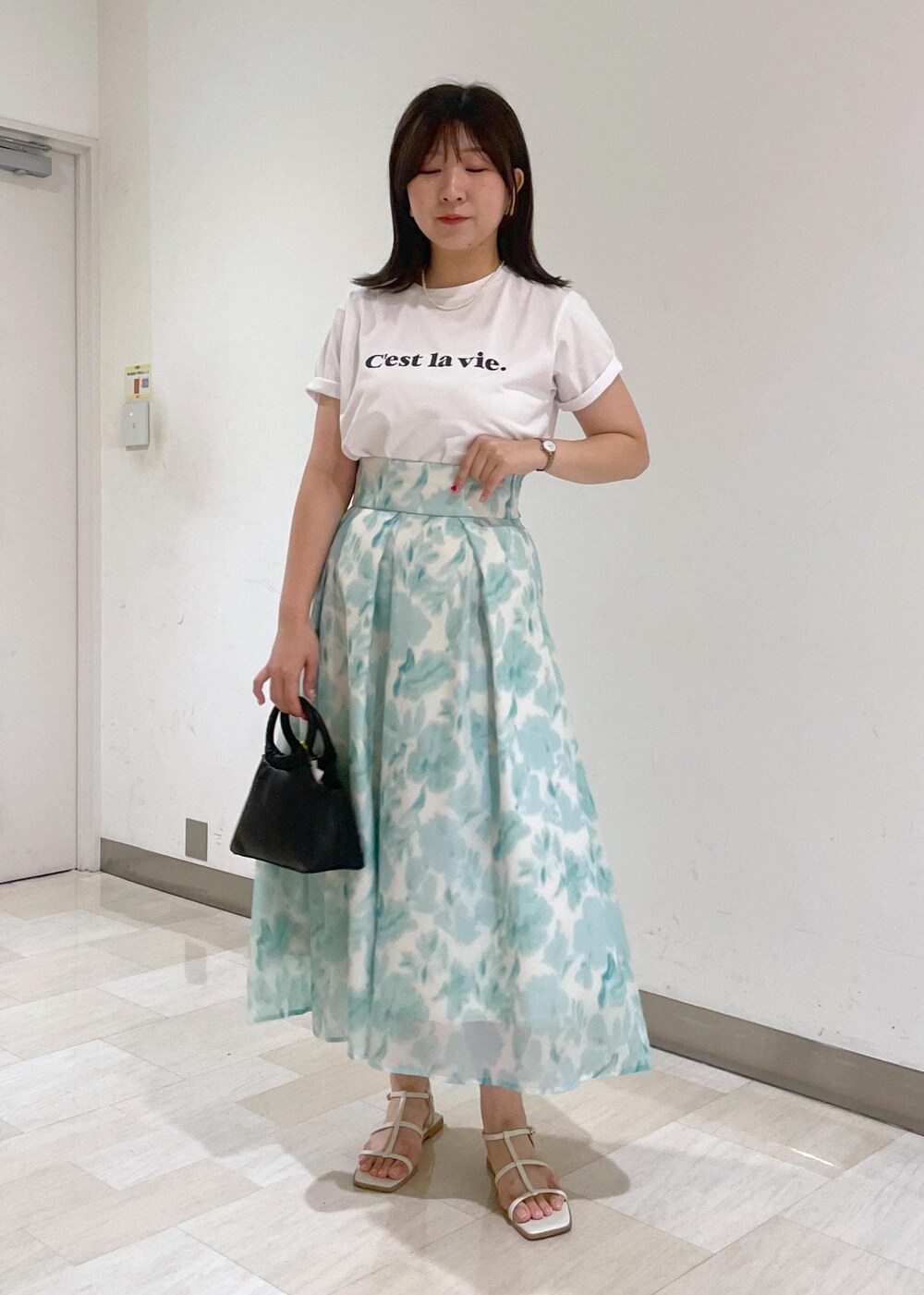 ブルー系のスカート、ブラック系のショルダーバッグ、ホワイト系のTシャツ/カットソーを着用したレディースの夏コーディネートの2枚目の写真