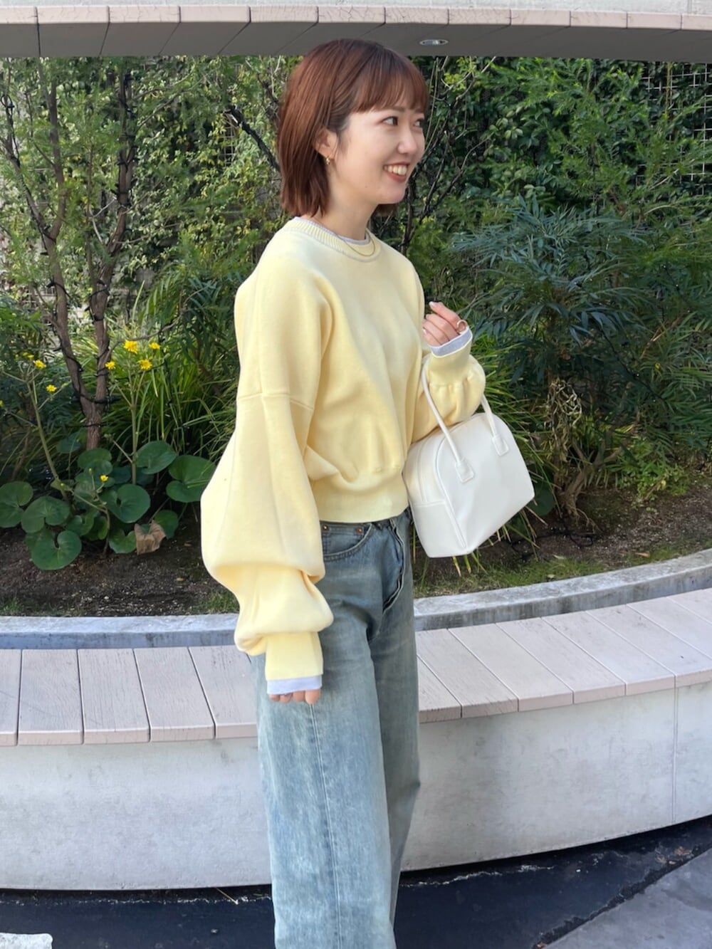 イエロー系のニット/セーター、ホワイト系のボストンバッグ、ブルー系のデニムパンツを着用したレディースの冬コーディネートの4枚目の写真