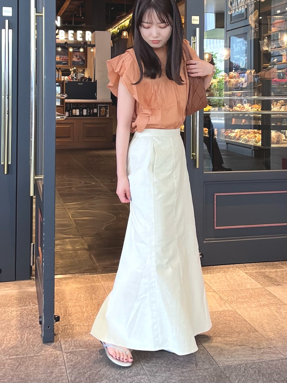 オレンジ系のシャツ/ブラウス、ホワイト系のスカートを着用したレディースの春コーディネートの2枚目の写真