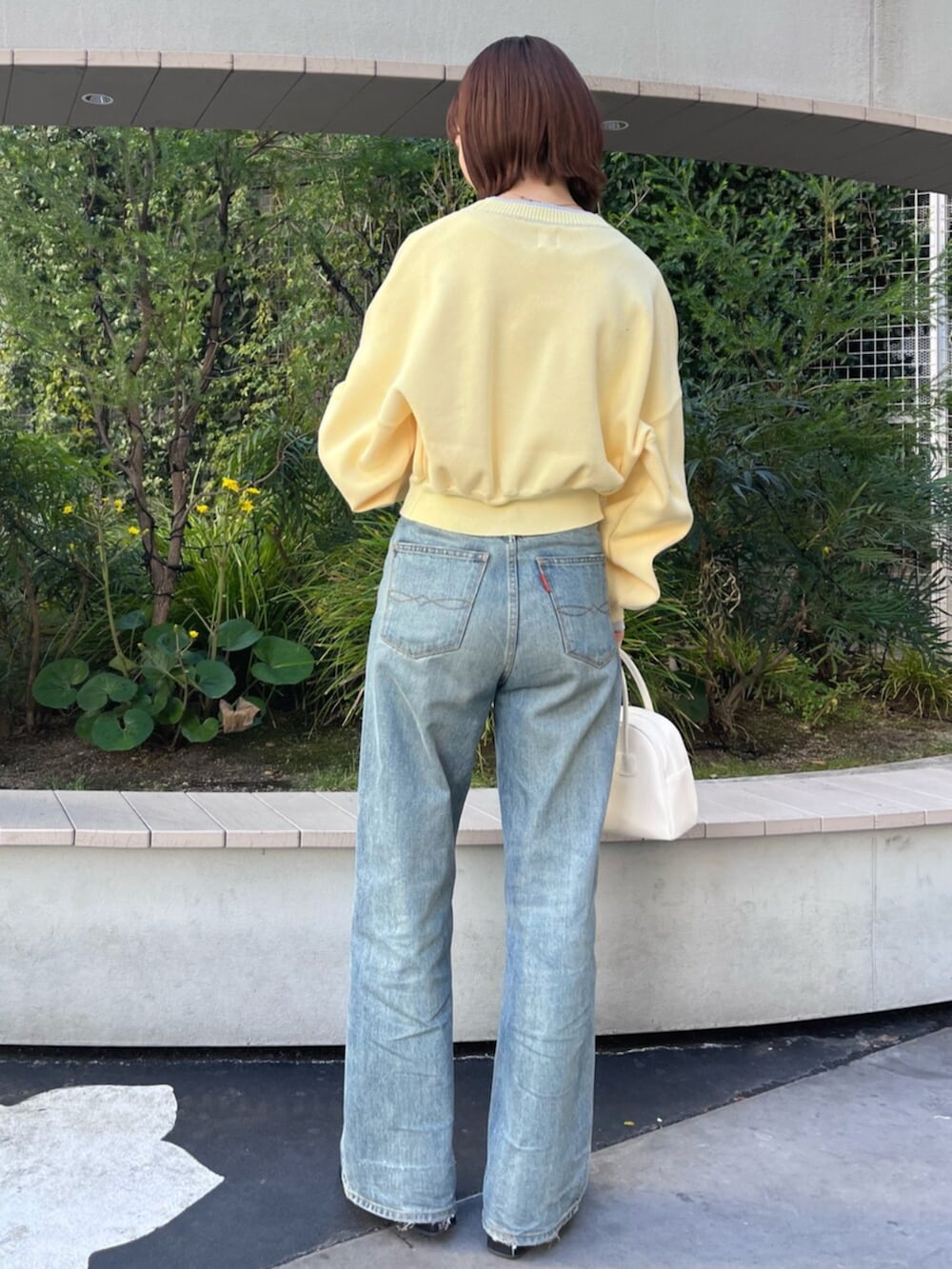 イエロー系のニット/セーター、ホワイト系のボストンバッグ、ブルー系のデニムパンツを着用したレディースの冬コーディネートの3枚目の写真