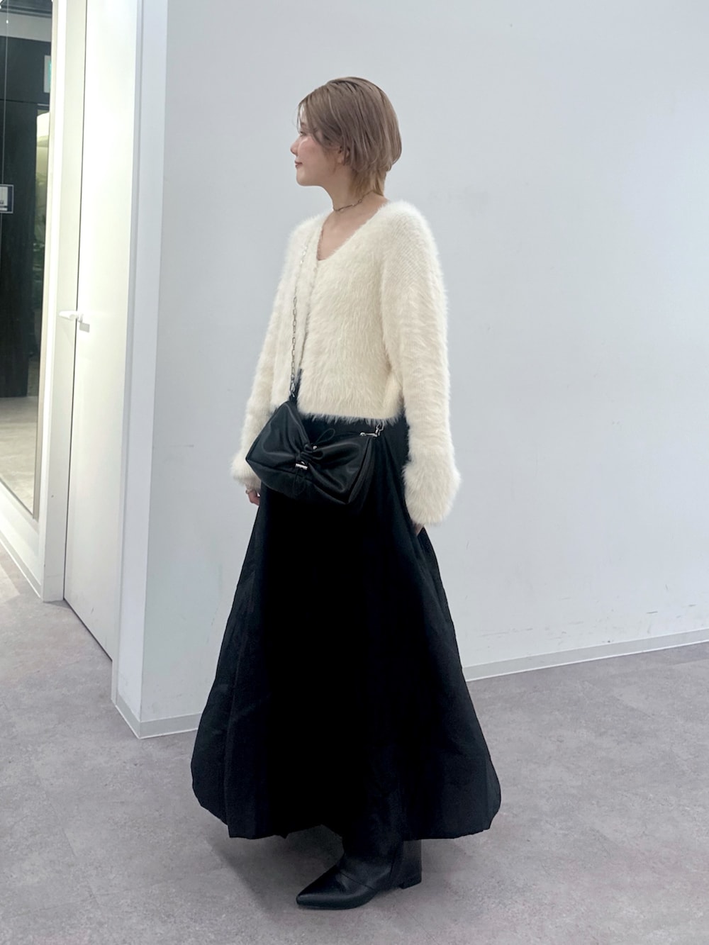 ホワイト系のカーディガン/ボレロ、ブラック系のスカート、ブラック系のハンドバッグを着用したレディースの秋コーディネートの3枚目の写真