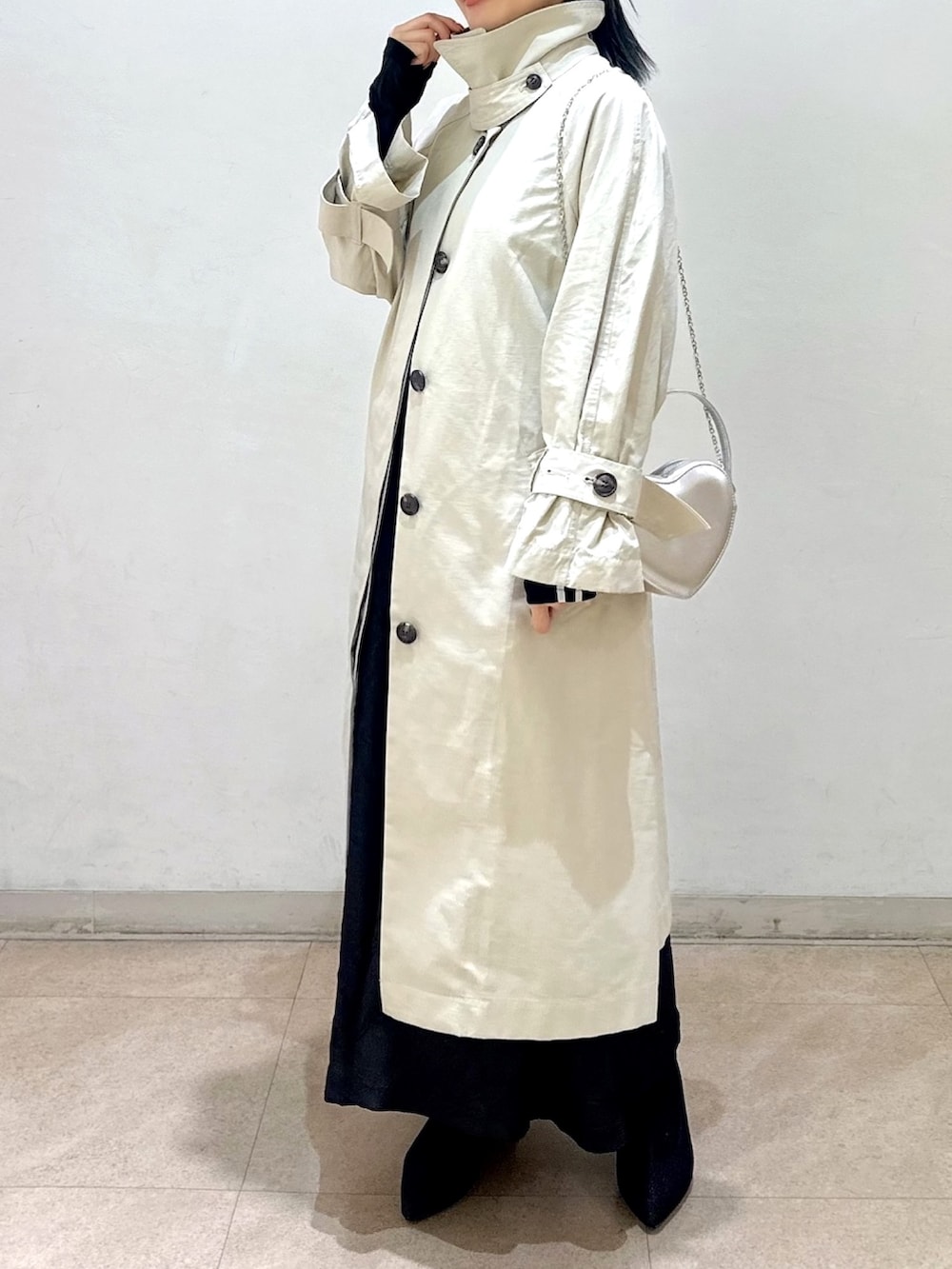 ベージュ系のトレンチコート、ブラック系のワンピース、ブラック系のTシャツ/カットソーを着用したレディースの春コーディネートの2枚目の写真