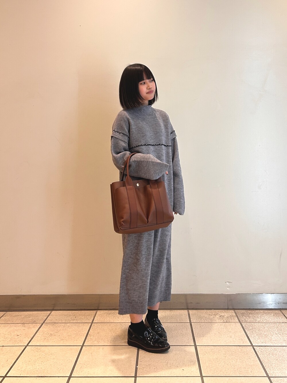 グレー系のワンピース、ブラウン系のショルダーバッグを着用したレディースの冬コーディネートの2枚目の写真