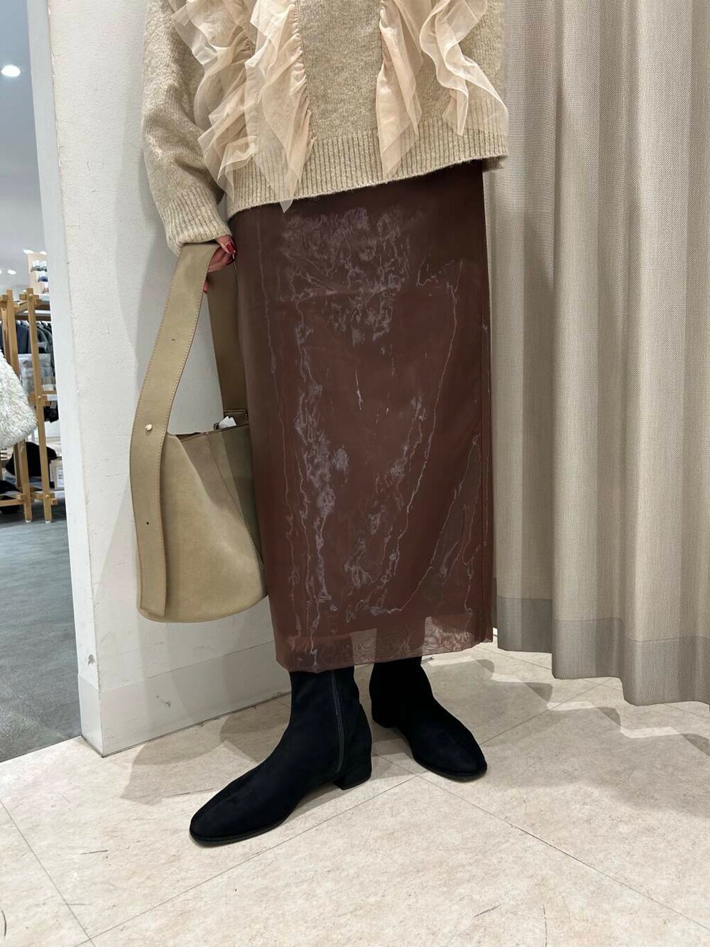 ベージュ系のハンドバッグ、ブラック系のブーツ、ブラウン系のスカートを着用したレディースの冬コーディネートの3枚目の写真