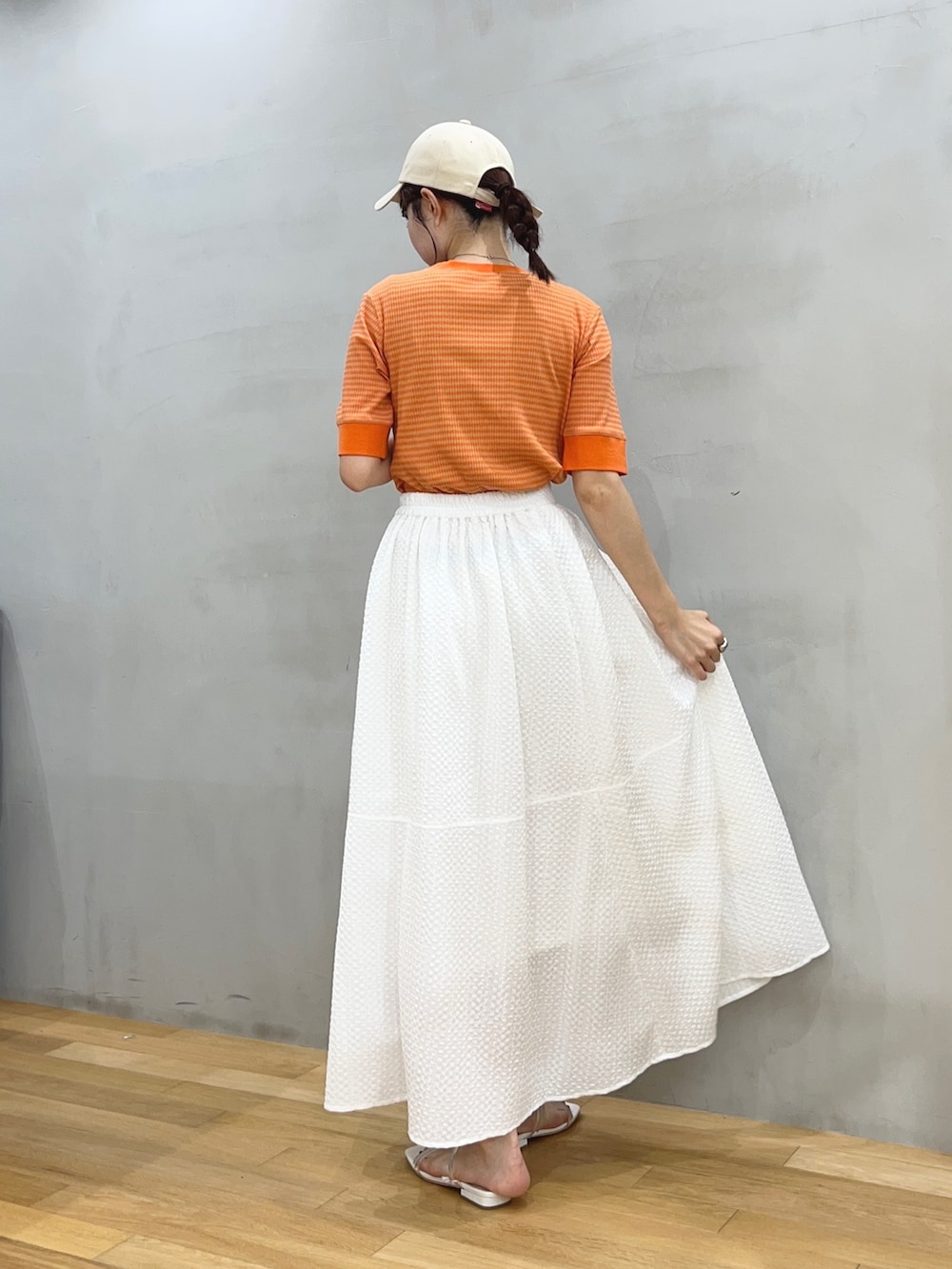 ホワイト系のスカート、オレンジ系のTシャツ/カットソー、ホワイト系のサンダルを着用したレディースの夏コーディネートの2枚目の写真