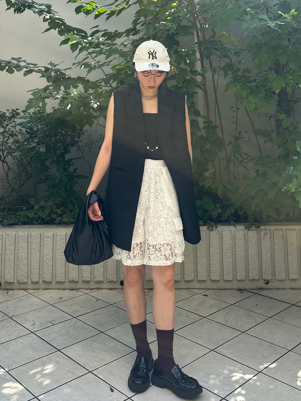 ブラック系のハンドバッグ、ブラック系のベスト、ホワイト系のパンツを着用したレディースの秋コーディネートの2枚目の写真