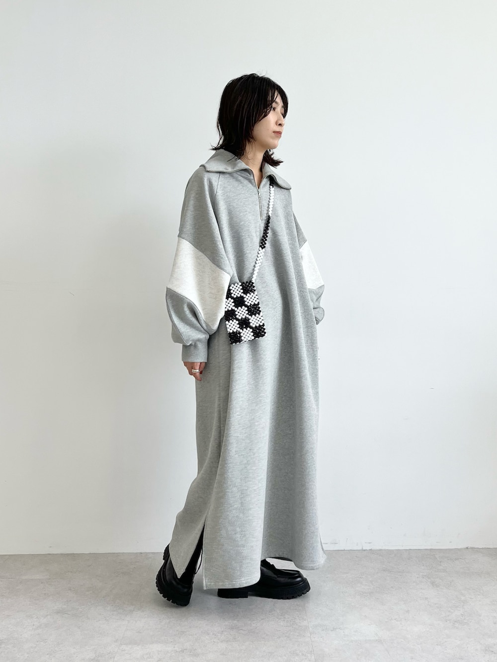 グレー系のワンピース、ブラック系のショルダーバッグ、ブラック系のブーツを着用したレディースの秋コーディネートの2枚目の写真