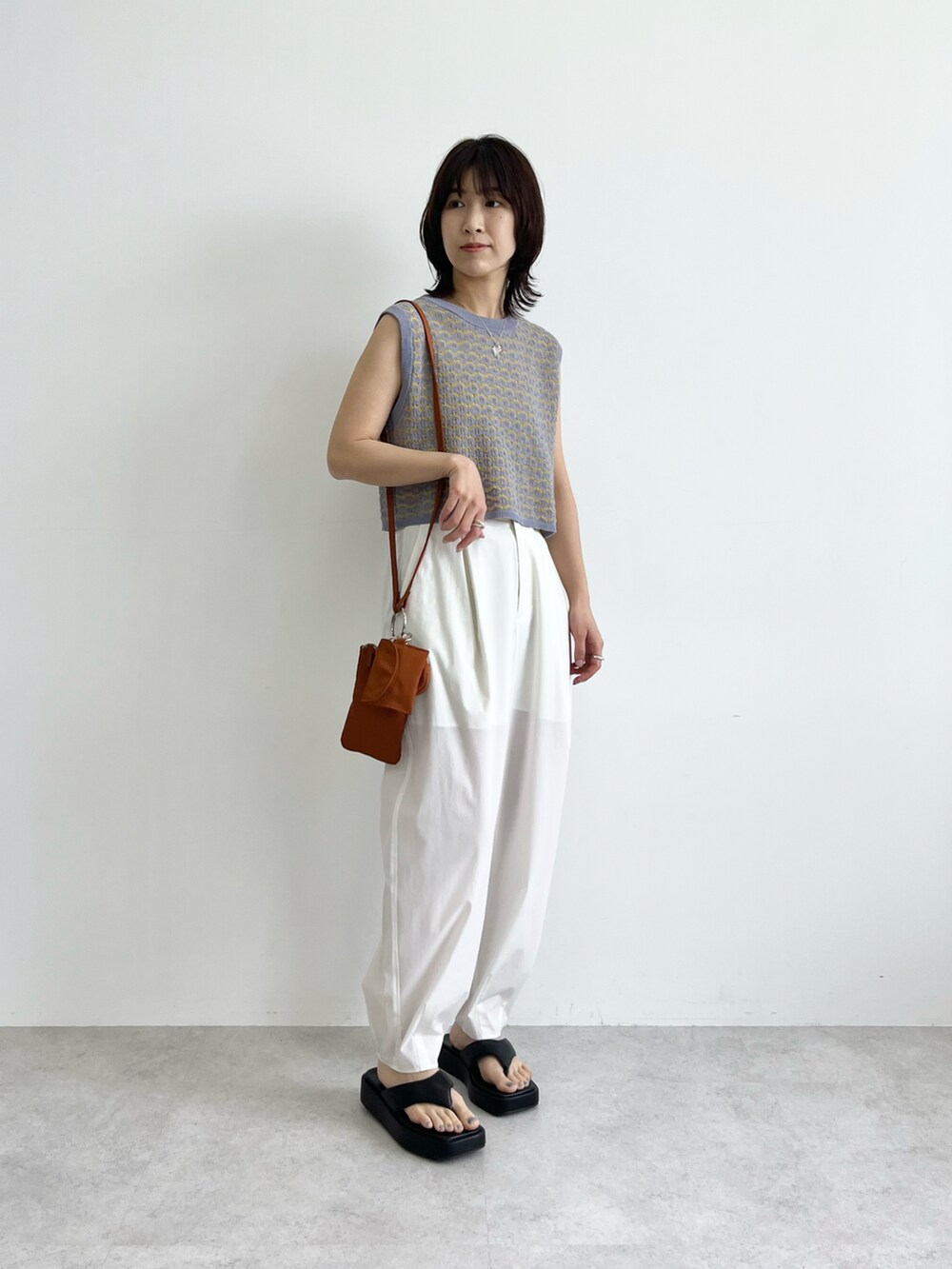 ブルー系のベスト、ブラウン系のショルダーバッグ、ホワイト系のその他パンツを着用したレディースの春コーディネートの2枚目の写真