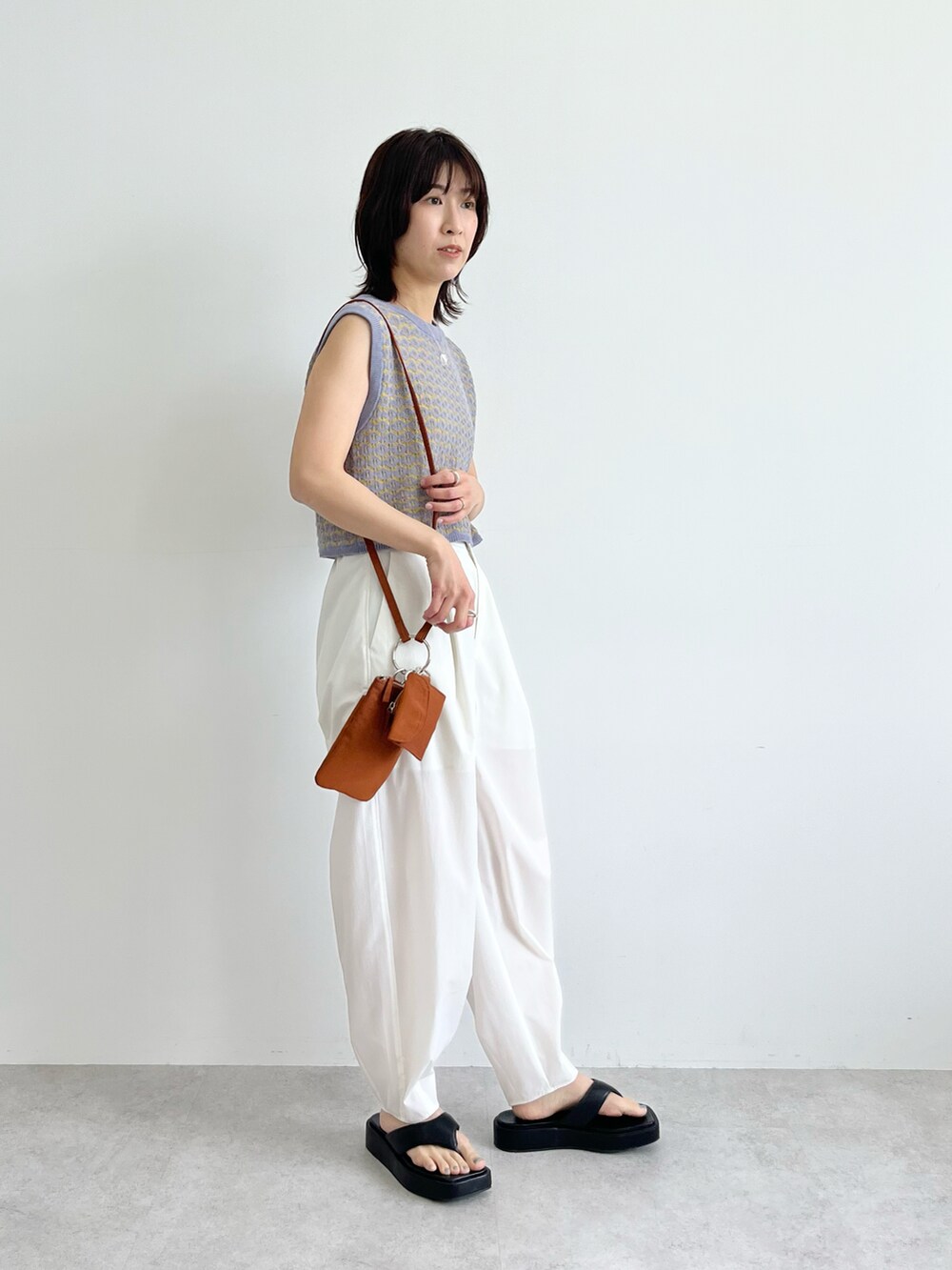 ブルー系のベスト、ブラウン系のショルダーバッグ、ホワイト系のその他パンツを着用したレディースの春コーディネートの3枚目の写真