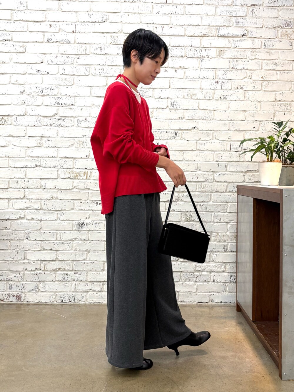 レッド系のニット/セーター、グレー系のTシャツ/カットソー、ブラック系のショルダーバッグを着用したレディースの秋コーディネートの2枚目の写真