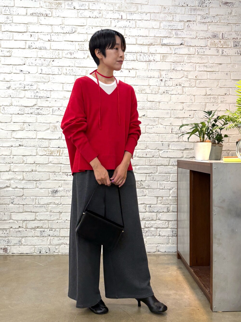 レッド系のニット/セーター、グレー系のTシャツ/カットソー、ブラック系のショルダーバッグを着用したレディースの秋コーディネートの5枚目の写真