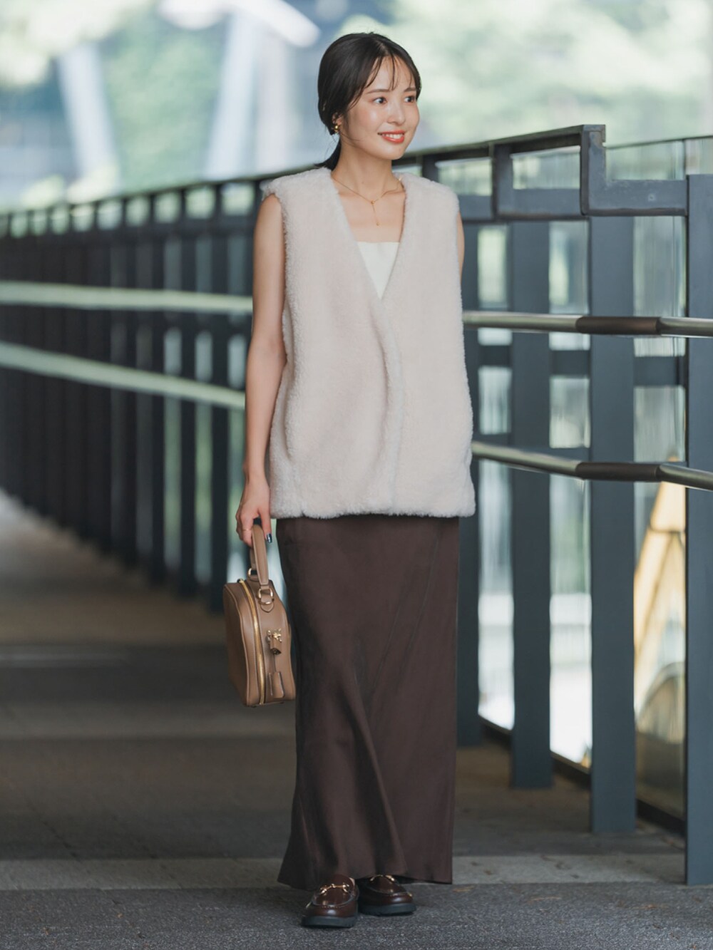 ホワイト系のベスト、ブラウン系のスカート、イエロー系のショルダーバッグを着用したレディースの秋コーディネートの2枚目の写真