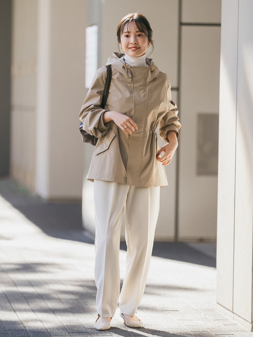 ベージュ系のマウンテンパーカー、ブラウン系のショルダーバッグ、ホワイト系のスラックスを着用したレディースの冬コーディネートの3枚目の写真