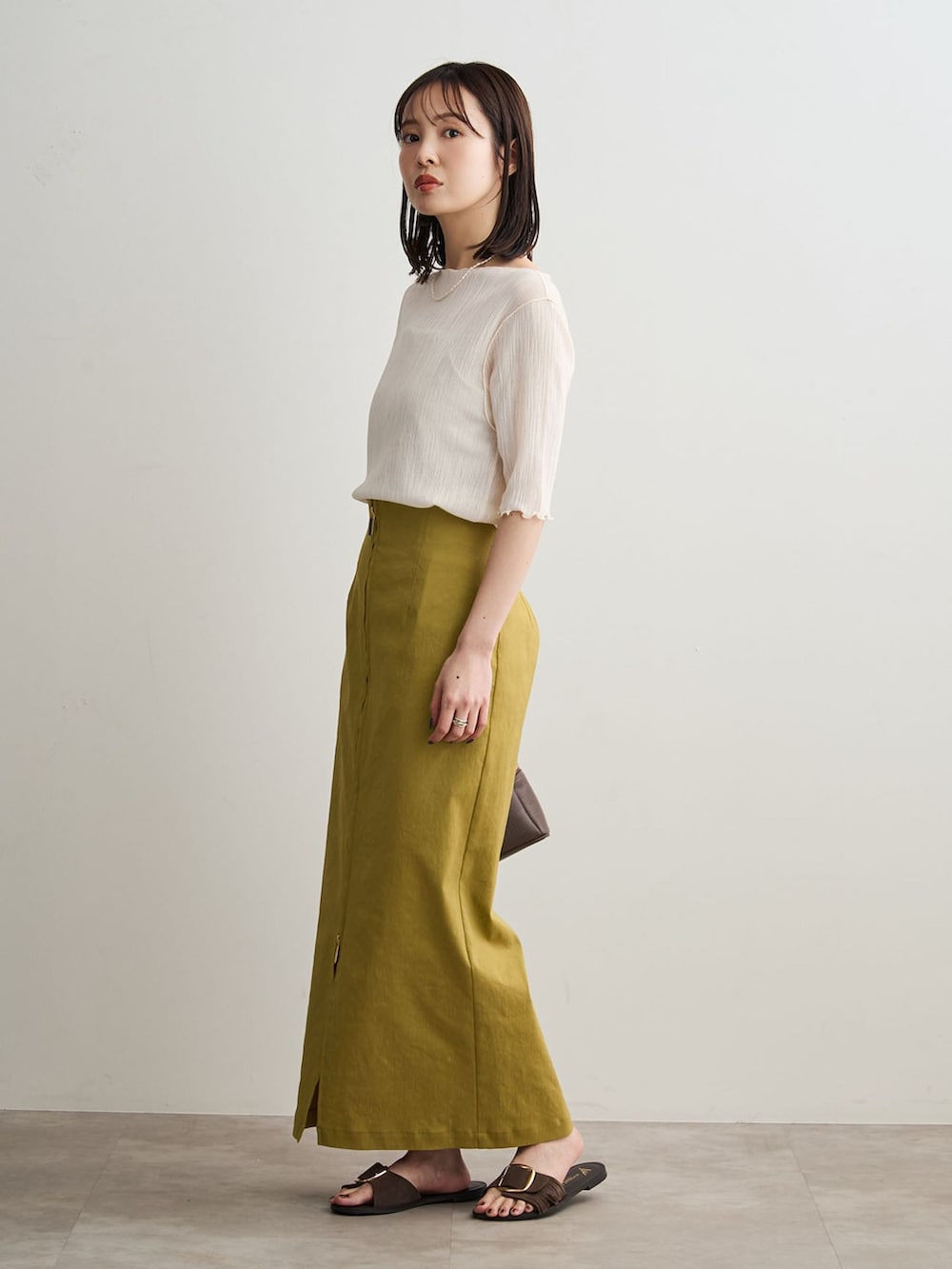 イエロー系のスカート、ホワイト系のTシャツ/カットソー、ブラウン系のショルダーバッグを着用したレディースの春コーディネートの2枚目の写真