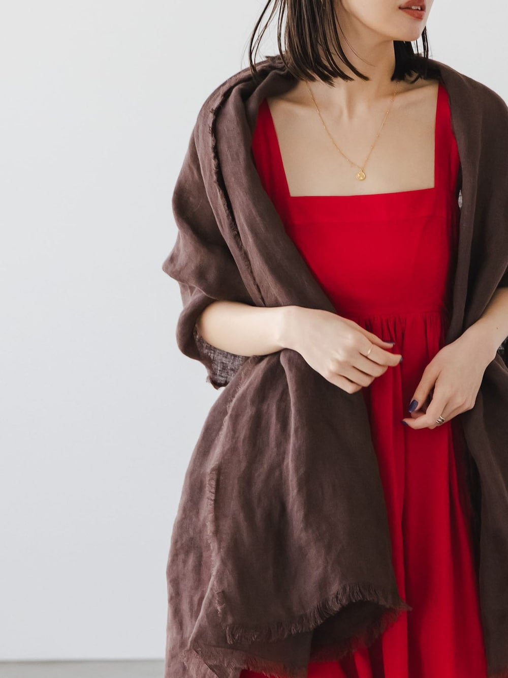 レッド系のワンピース、ゴールド系のネックレス、ブラウン系のストール/ショールを着用したレディースの春コーディネートの4枚目の写真