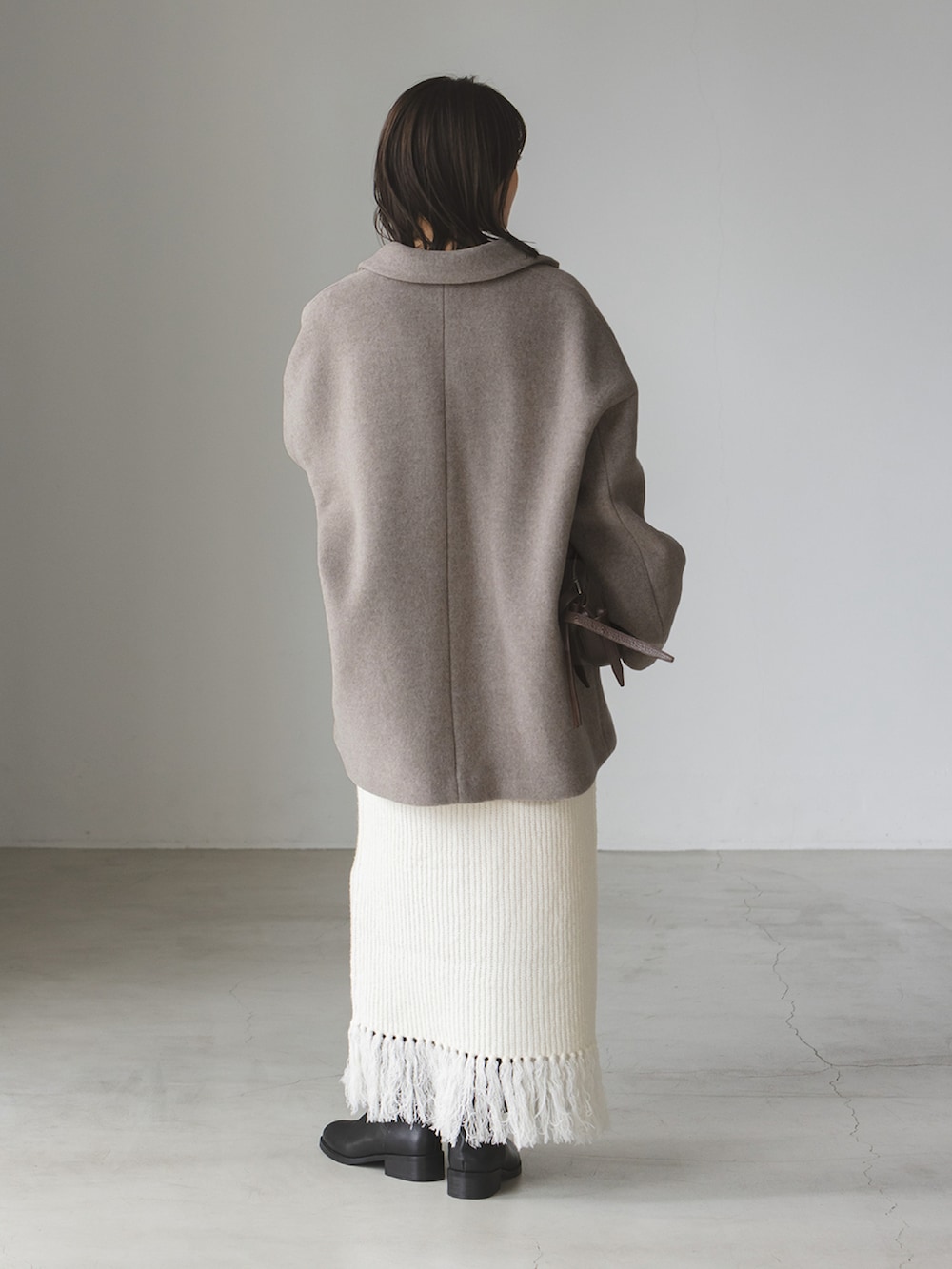 ベージュ系のピーコート、ホワイト系のスカート、ブラウン系のショルダーバッグを着用したレディースの秋コーディネートの2枚目の写真