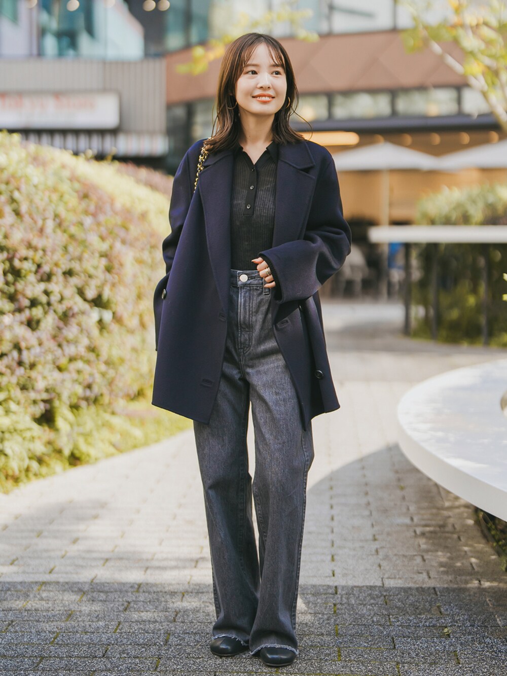 ブルー系のチェスターコート、ブラック系のデニムパンツ、ブラック系のブーツを着用したレディースの秋コーディネートの2枚目の写真