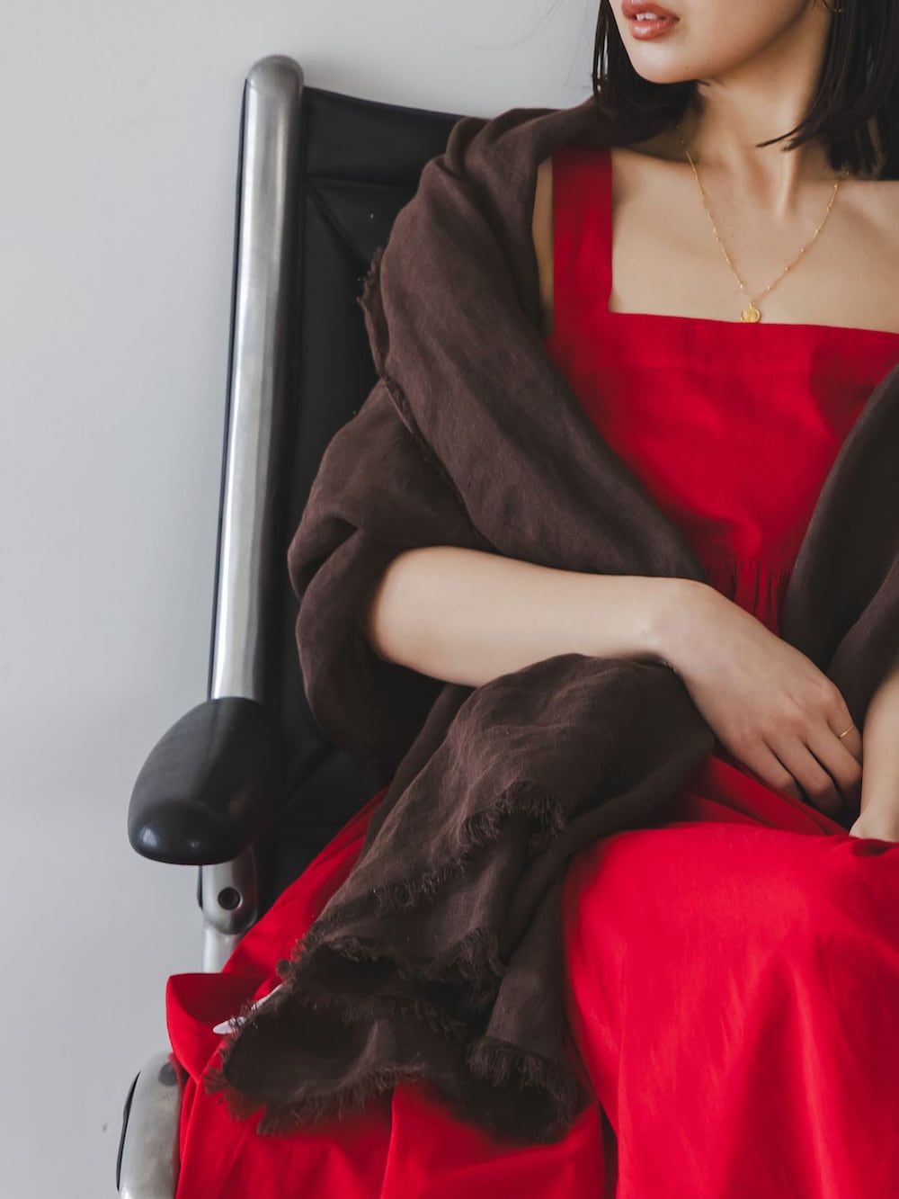 レッド系のワンピース、ゴールド系のネックレス、ブラウン系のストール/ショールを着用したレディースの春コーディネートの3枚目の写真