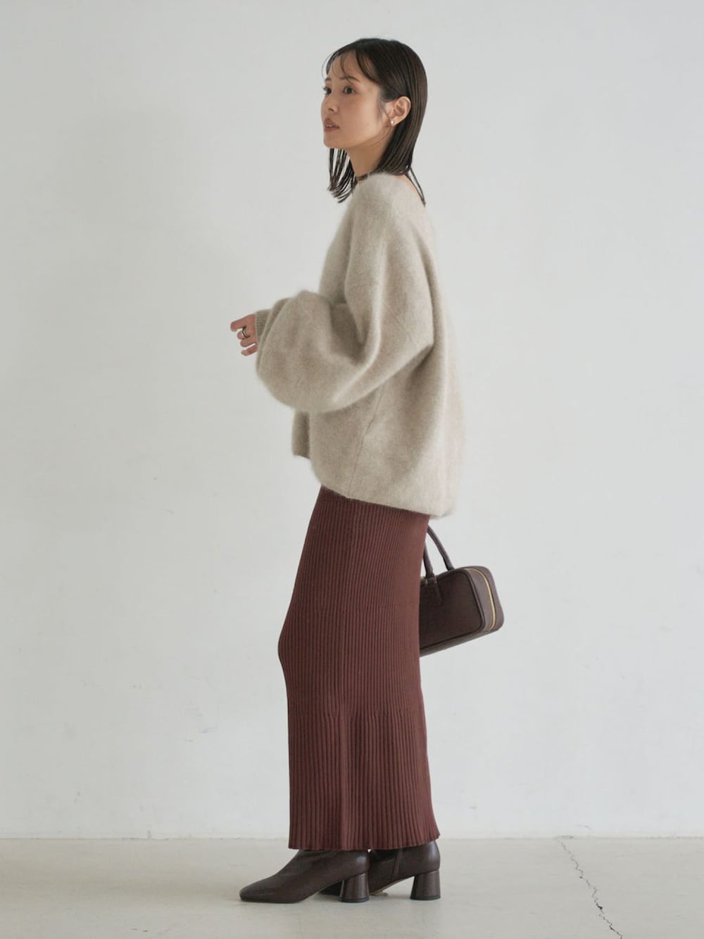 ベージュ系のニット/セーター、ブラウン系のスカート、ブラウン系のブーツを着用したレディースの秋コーディネートの2枚目の写真